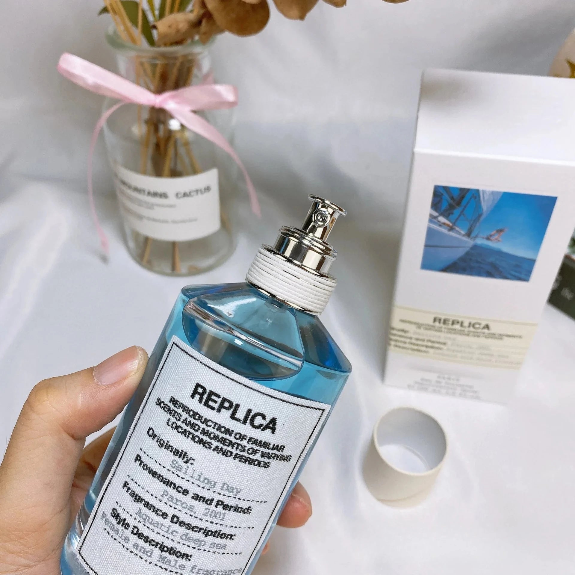 A blue bottle of 100ml Unisex Pheromone Perfume Long Lasting Woody Floral Natural Fragrance, with a silver nozzle and sailboat label, next to a small gift box